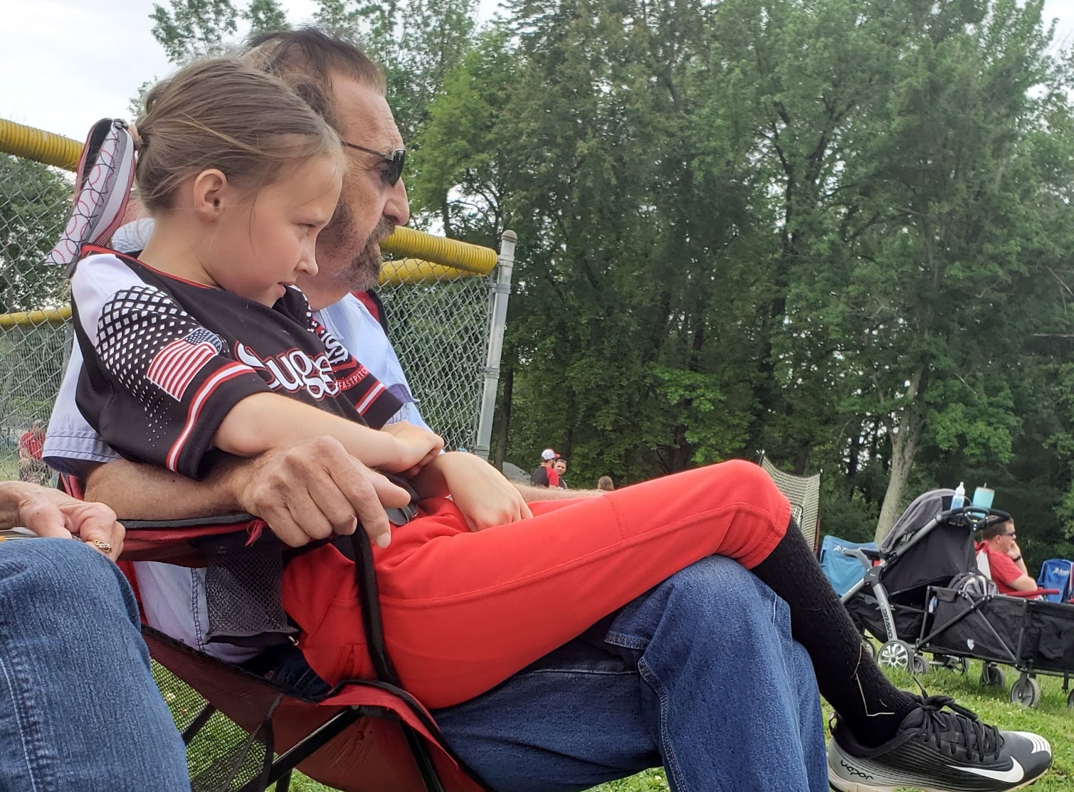 Grandpa Paul-Paul holds Aubrie as they watch a softball game together